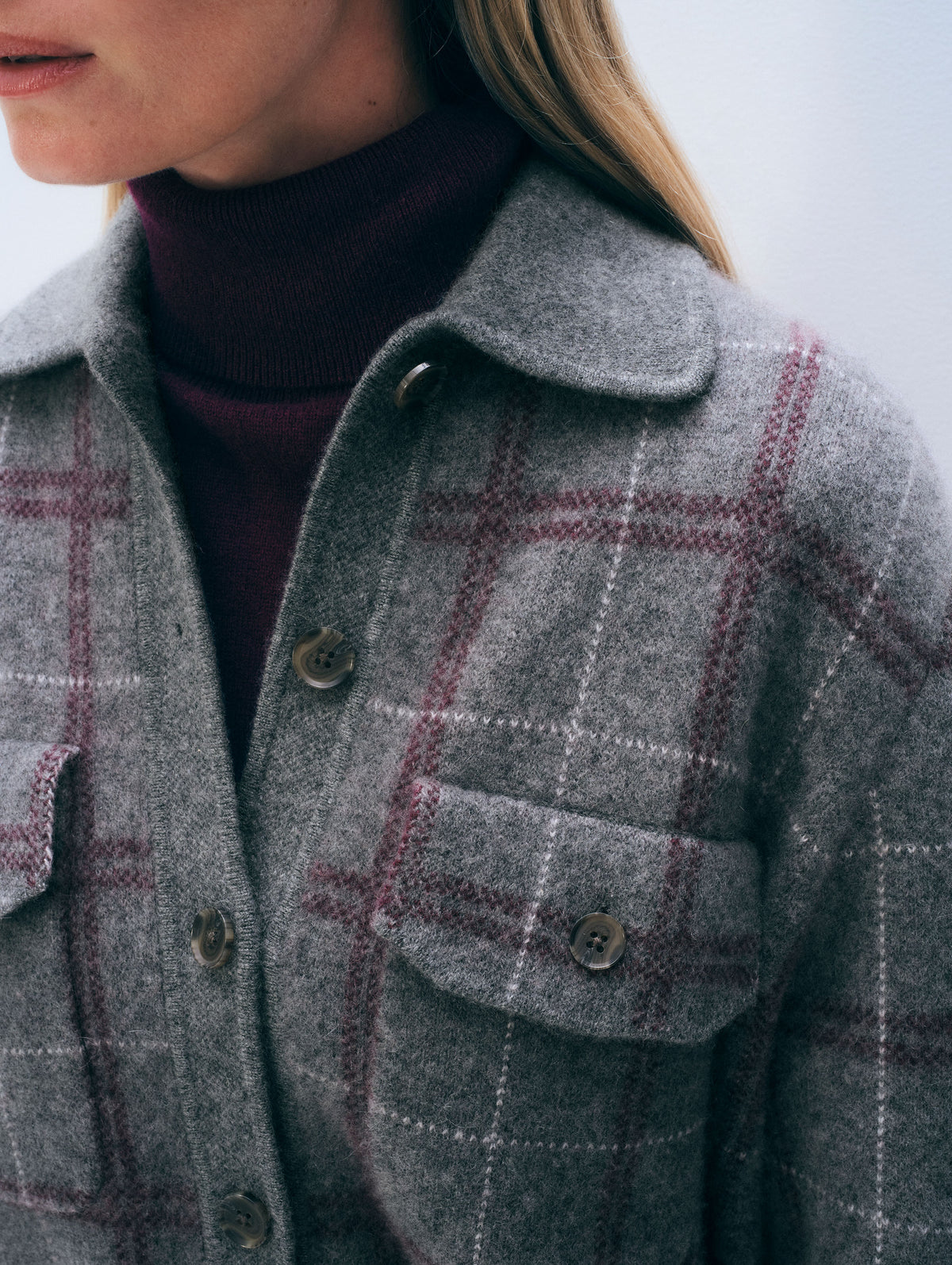 Close-up of a person wearing a gray wool-like plaid button-front jacket over a dark burgundy turtleneck sweater.