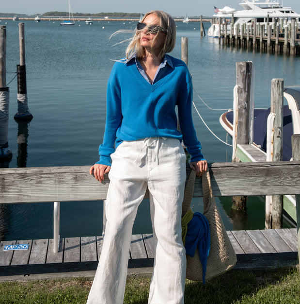 Woman in blue sweater and white pants standing on a dock by the water