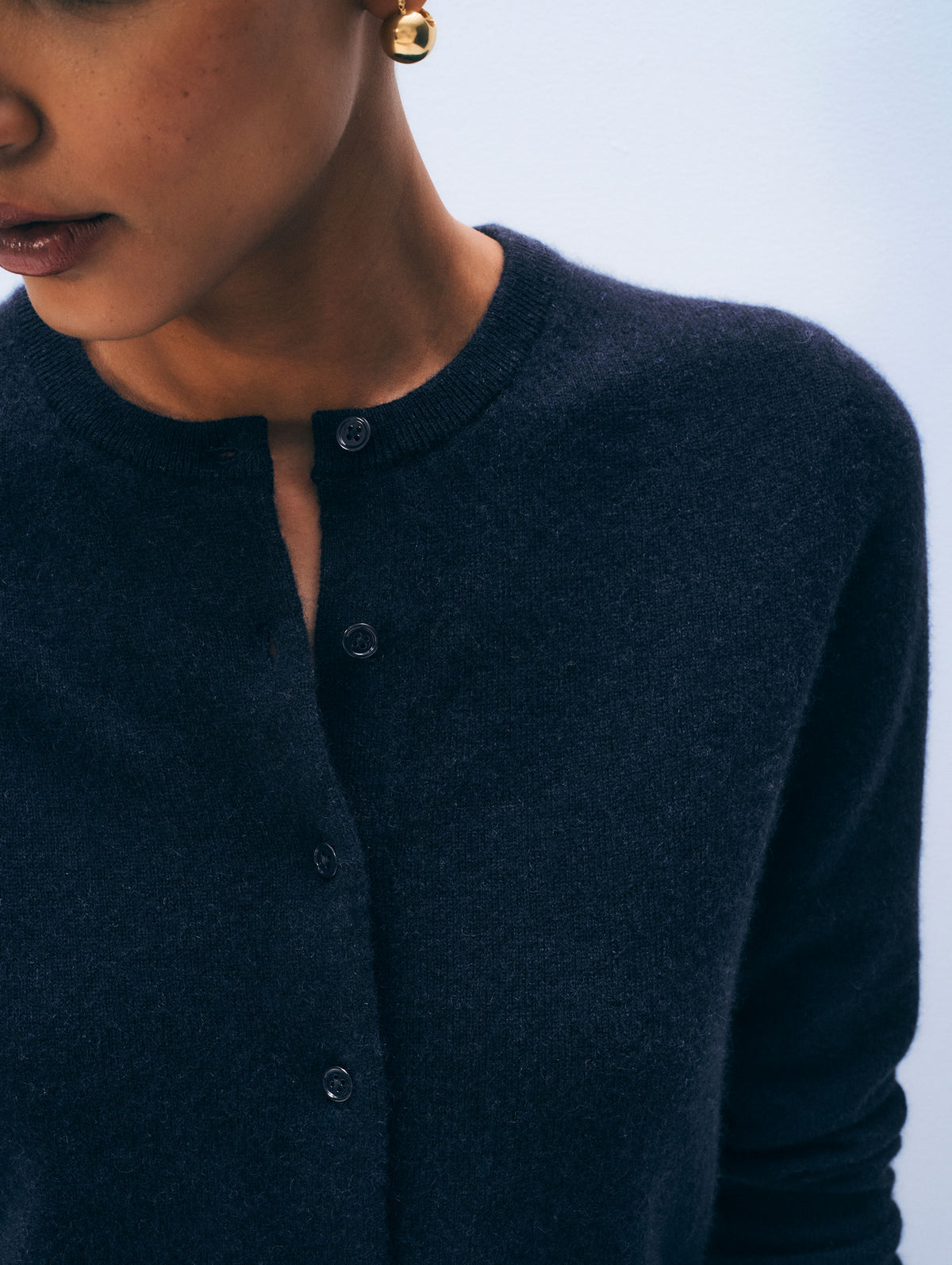 Close-up of a person wearing a dark navy knit cardigan with a buttoned neckline, against a pale blue background.