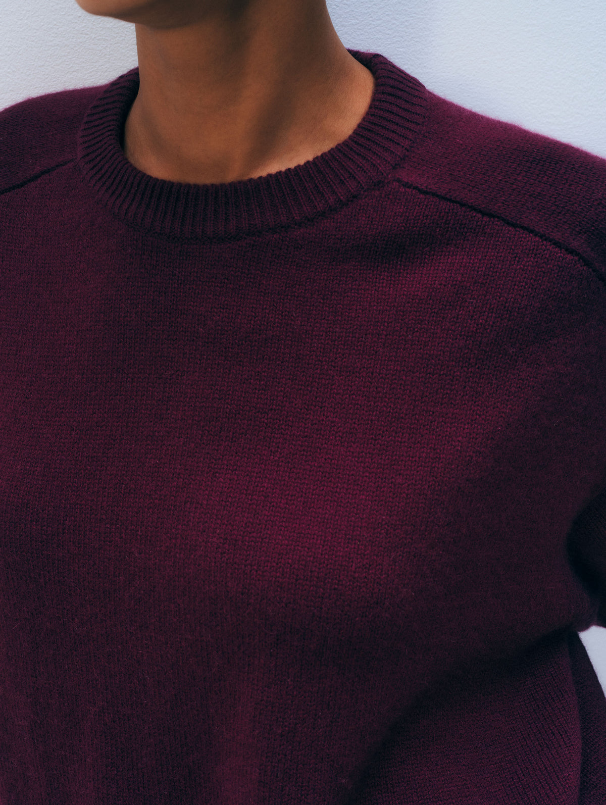 Close-up of a person wearing a ribbed crewneck sweater in deep burgundy or maroon, showing the knit texture and collar against a plain light background.