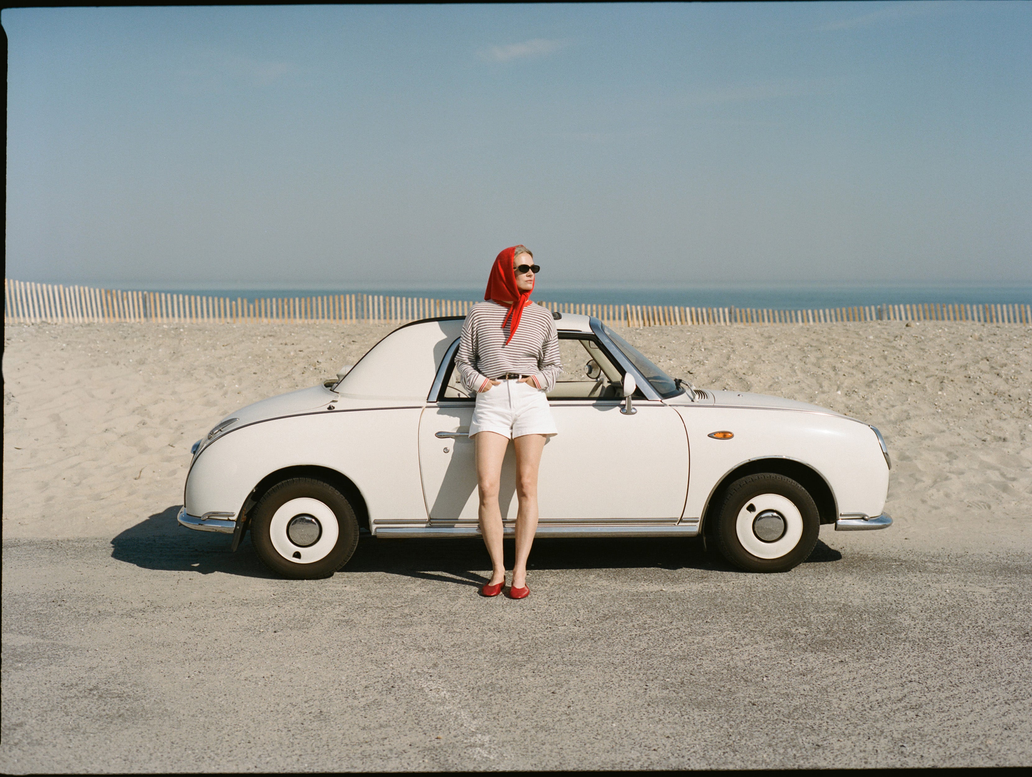 Woman standing next to a vintage car on a beach