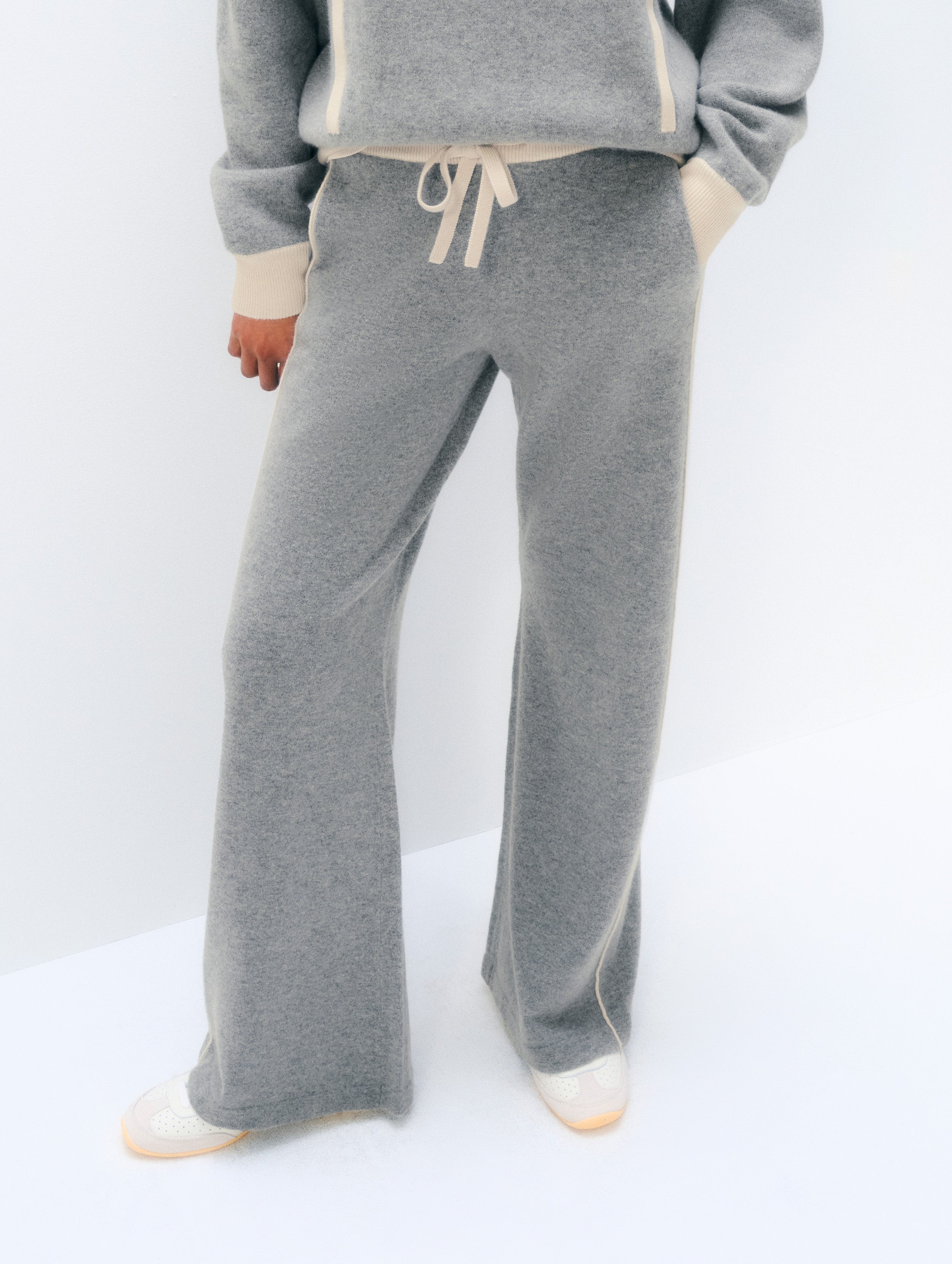 A person wearing heather gray wide-leg sweatpants with cream drawstrings and matching gray and cream knit top, photographed against a clean white studio background.