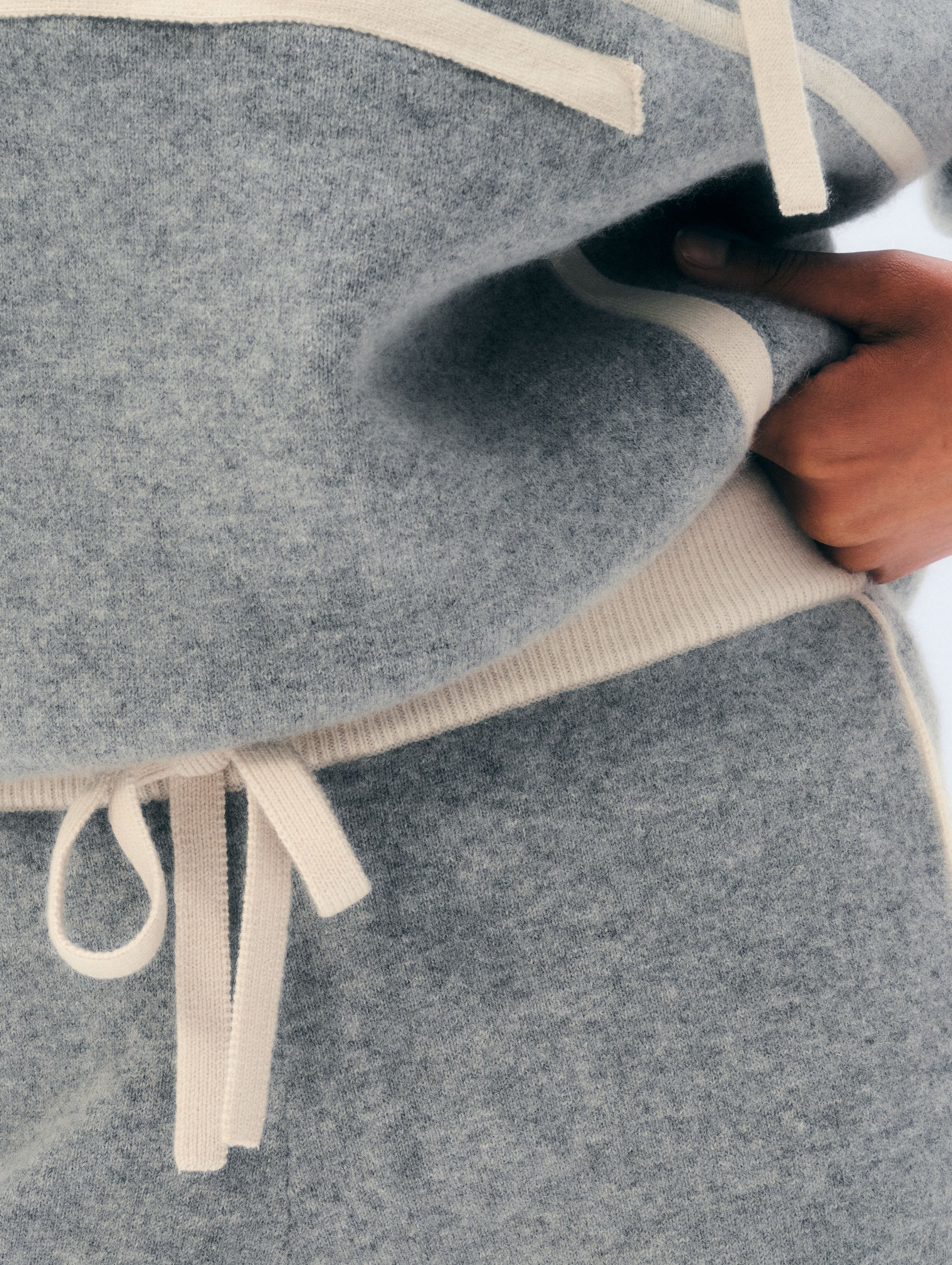 Close-up of a gray knit fabric item with cream-colored ribbed trim and drawstring ties, being held by a hand.