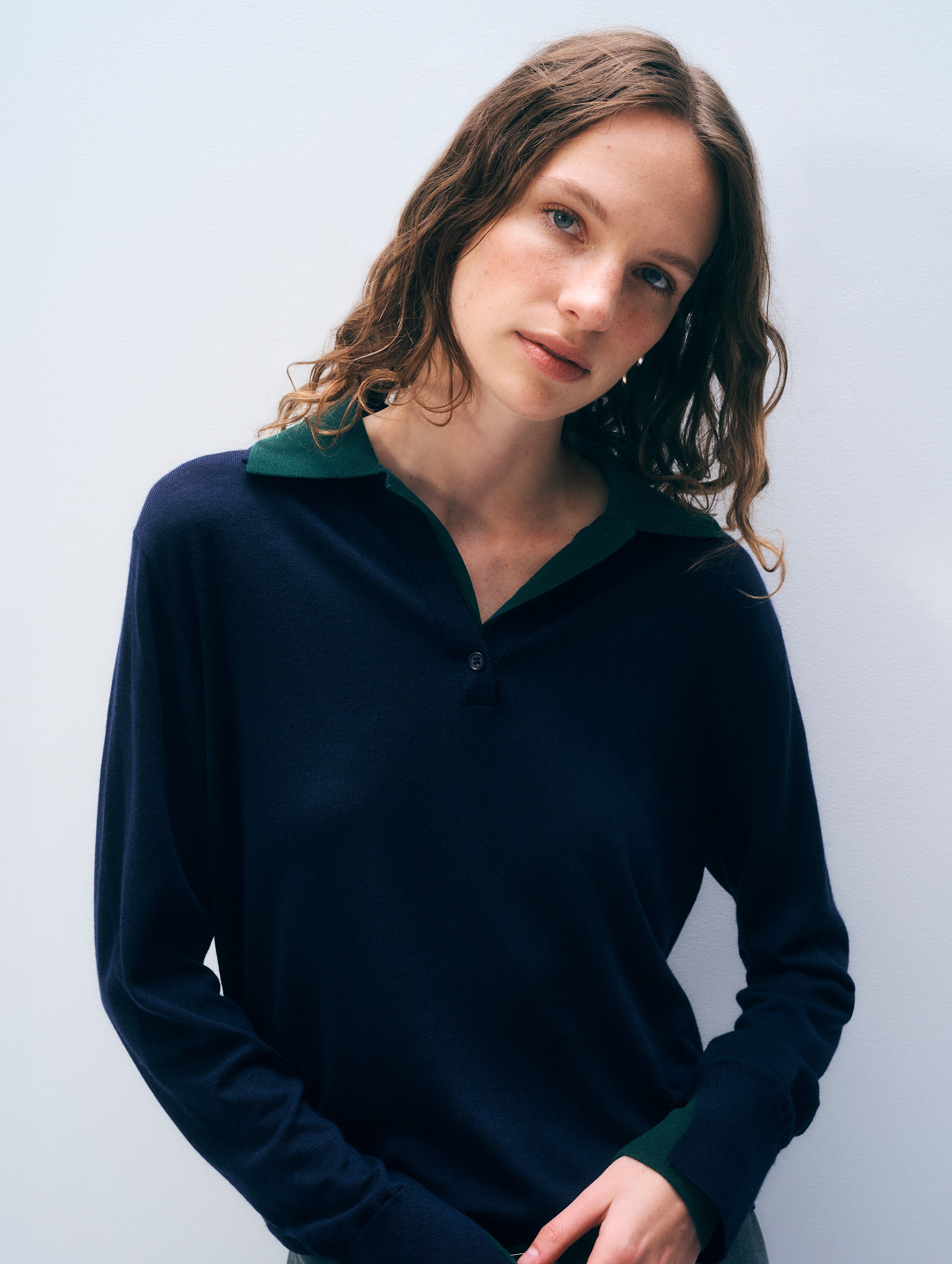 A woman wearing a dark navy long-sleeve polo sweater with a contrasting dark green inner collar, photographed against a light gray studio background.