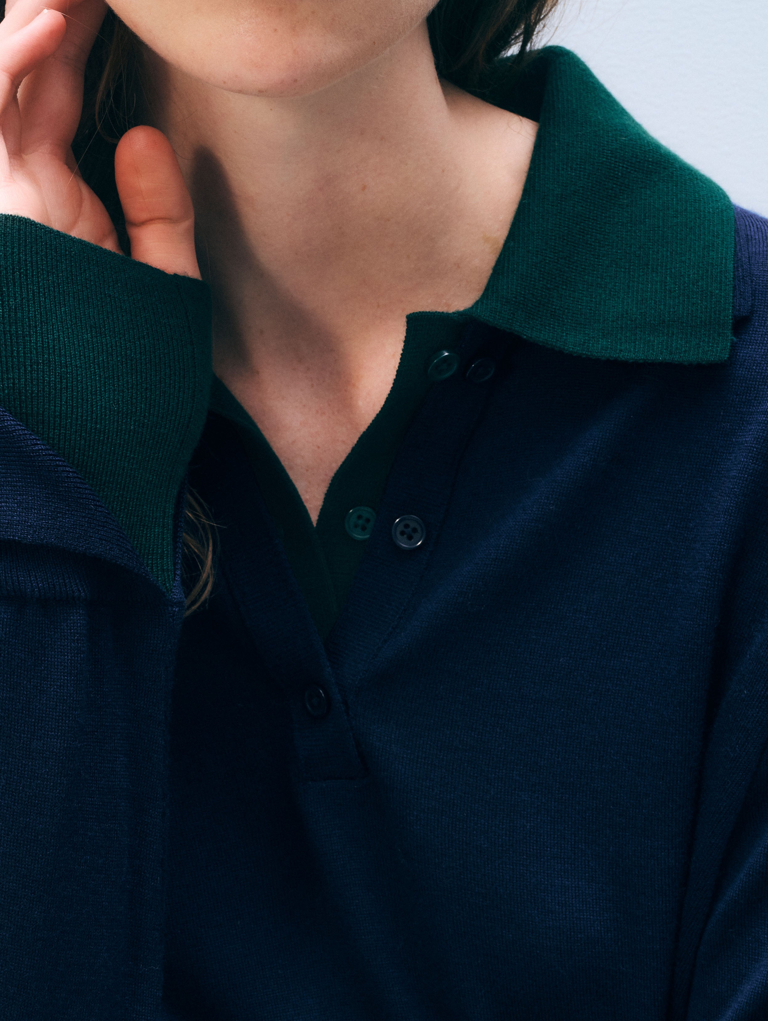 Close-up of a person wearing a dark navy polo shirt with a contrasting dark green collar and matching green ribbed placket.