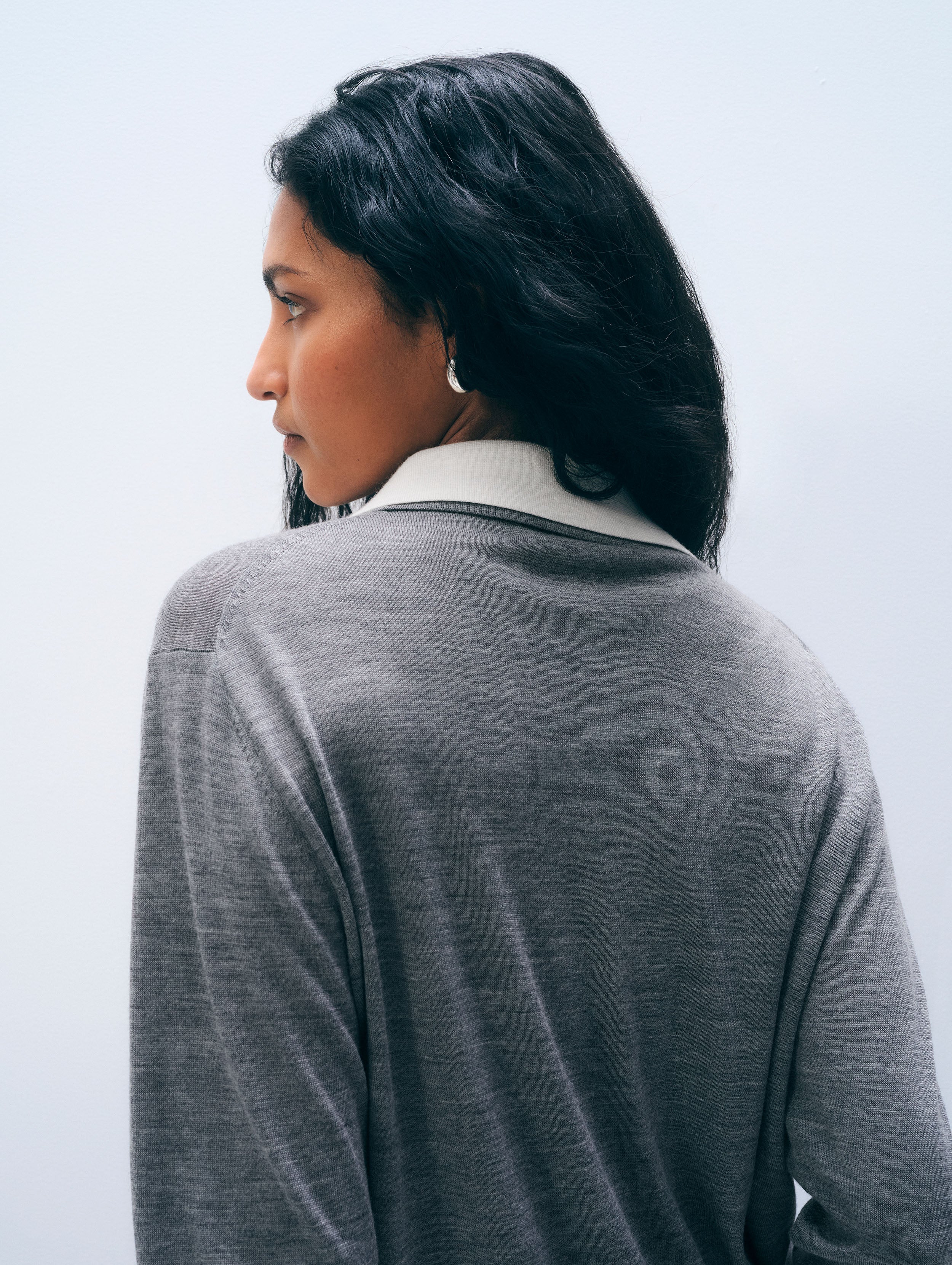 A woman shown from the back wearing a heather gray long-sleeve top with a contrasting white collar, set against a plain light gray background.