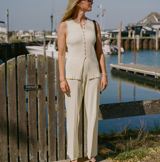 Woman in a beige outfit standing by a dock with boats in the background